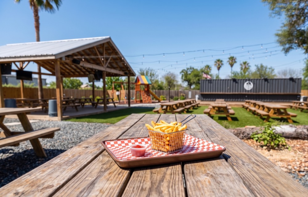 Sunny outdoor picnic-table seating and playground at GW's BBQ